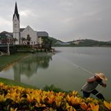 Ein Arbeiter sprüht Wasser auf die Blumen, die den Nachbau des österreichischen Ortes Hallstatt umranden. Das Stahlunternehmen Minmetals ließ die Wohnsiedlung vor mehr als zehn Jahren für knapp eine Milliarde Euro in der Stadt Luoyangzhen in Südchina errichten. Zur Eröffnung reiste auch der Bürgermeister des echten Hallstatt an, ein Ort im Salzkammergut, den die UNESCO zum Weltkulturerbe ernannt hat. Statt einer Alpenkulisse ragen auf der anderen Seite des Sees Hochhäuser in den Himmel