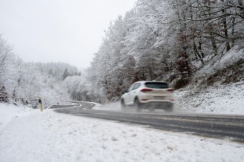 Ein weißer SUV fährt auf einer vereisten Straße durch eine winterliche triste Landschaft