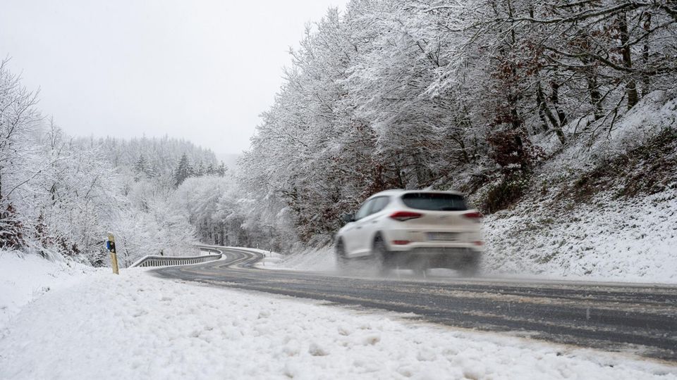 Ein weißer SUV fährt auf einer vereisten Straße durch eine winterliche triste Landschaft