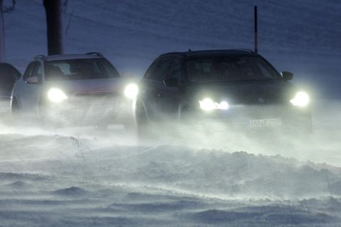 Autos mit eingeschalteten Scheinwerfern fahren in Kolonne über eine Straße mit Schnee und Glätte