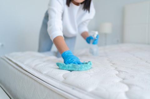 Frau besprüht Matratzentuch mit speziellen Reinigungsmitteln, um Flecken zu entfernen