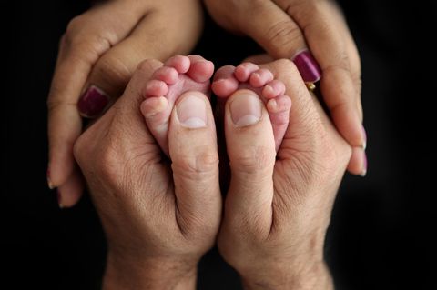 Die Hände eines Mannes und einer Frau umfassen ein Paar winziger Babyfüße