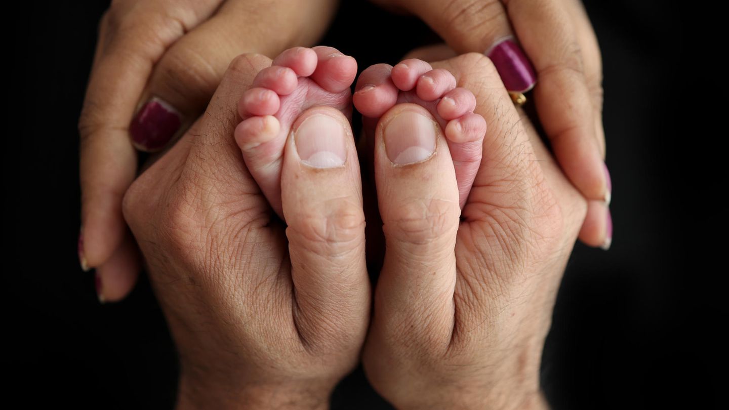 Die Hände eines Mannes und einer Frau umfassen ein Paar winziger Babyfüße