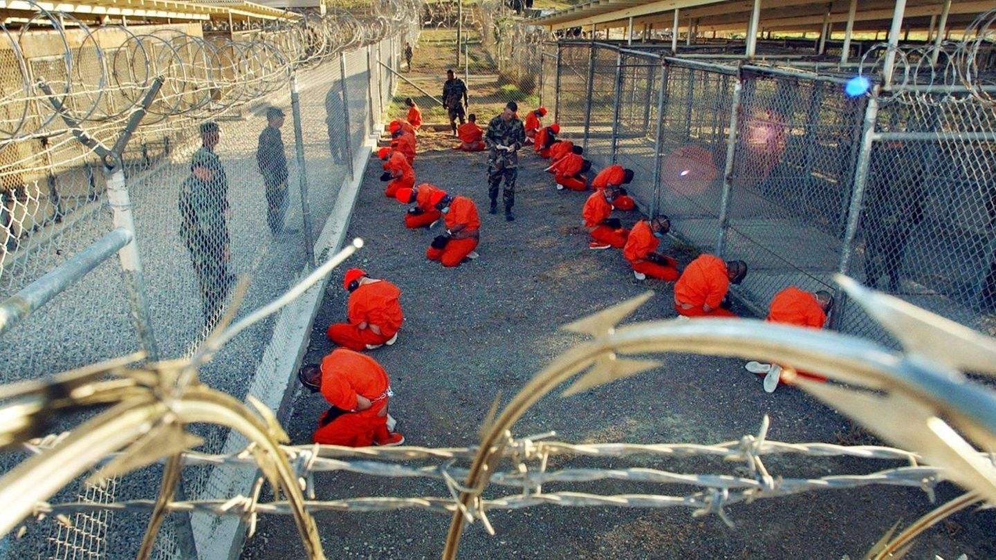 In orangefarbene Overalls gekleidete Häftlinge, die in Guantánamo Bay auf Kuba auf dem Boden knien