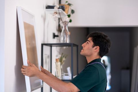Junger Handwerker hängt zu Hause ein leeres Gemälde an die Wand