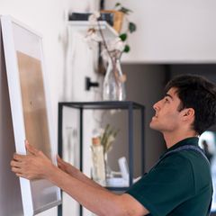 Junger Handwerker hängt zu Hause ein leeres Gemälde an die Wand