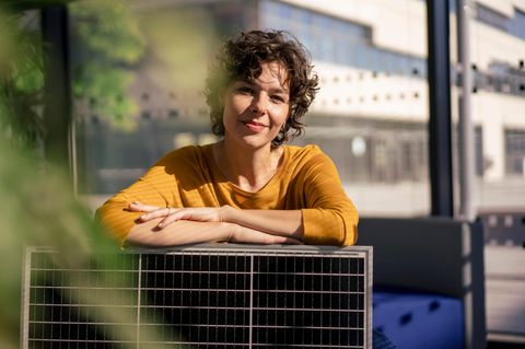 Frau lehnt über einem Balkonkraftwerk und lächelt in die Sonne.