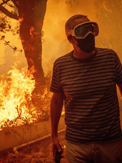 Mit Atemmaske und Schutzbrille steht ein Mann auf seinem Grundstück in Pacific Palisades. Die Flammen sind bereits gefährlich nah