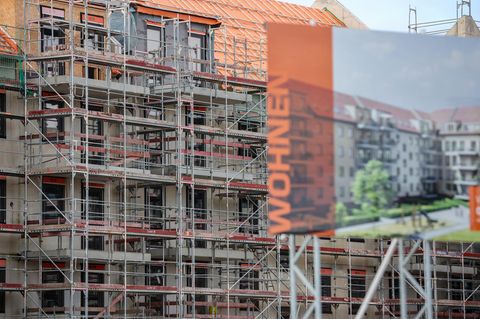 Eine Bautafel steht vor der Baustelle mehrerer Miethäuser