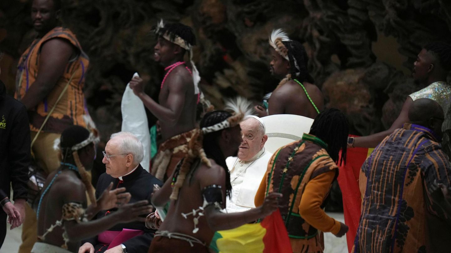 Papst Franziskus sitzt, während um ihn herum eine afrikanische Zirkustruppe tanzt