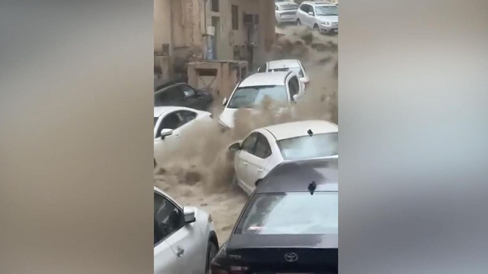 Mehrere Autos werden von großen schlammigen Wassermassen eine Straße herunter gespült