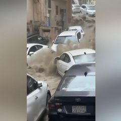 Mehrere Autos werden von großen schlammigen Wassermassen eine Straße herunter gespült