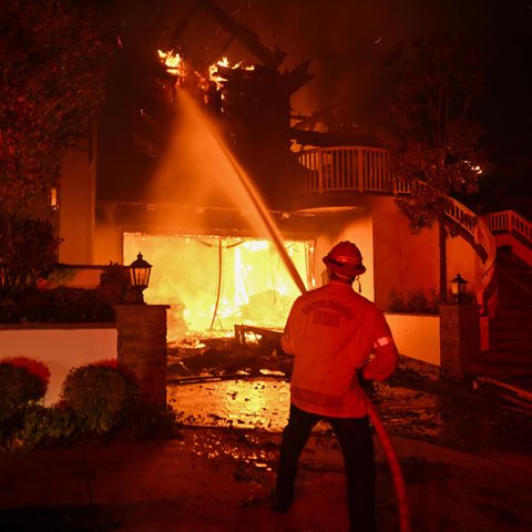 Los Angeles: Ein Feuerwehrmann steht mit einem Wasser sprühenden Schalauch vor einem brennenden Haus