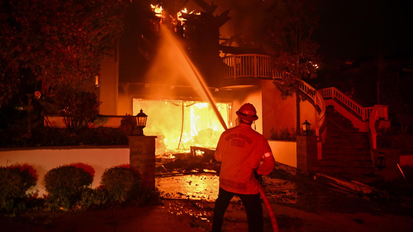 Los Angeles: Ein Feuerwehrmann steht mit einem Wasser sprühenden Schalauch vor einem brennenden Haus