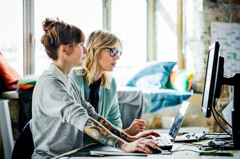 Zwei Frauen sitzen vor einem Laptop und PC-Bildschirm