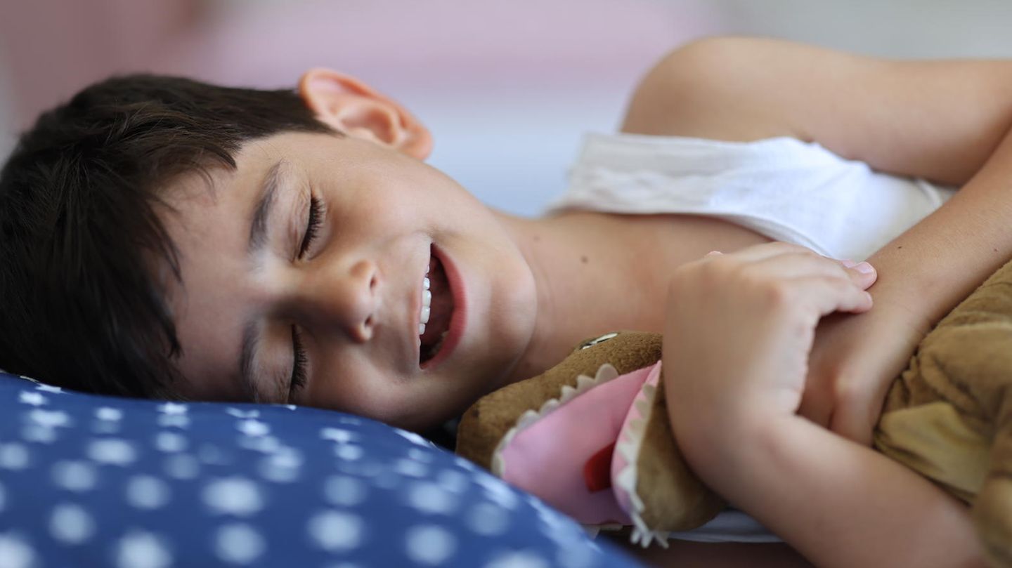Kinderwünsche: Ein Junge liegt lächelnd mit geschlossenen Augen im Bett