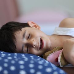Kinderwünsche: Ein Junge liegt lächelnd mit geschlossenen Augen im Bett