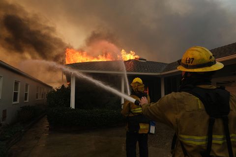 Zwei Feuerwehrmänner versuchen ein brennendes Haus zu löschen