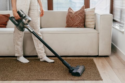 Person, die ein gemütliches Wohnzimmer mit modernem Design staubsaugt