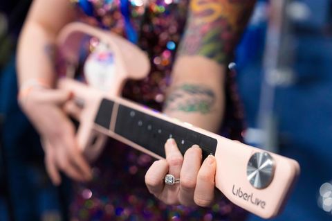 Eine Frau hält den Gitarrenhals einer rosafarbenen, saitenlosen Gitarre