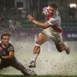 Sportfoto: Zwei Rugbyspieler bei einem regnerischen Spiel – einer fällt hin, der andere rennt mit dem Ball davon