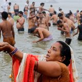 Eine Frau betet, während sie ein Bad im Sangam nimmt