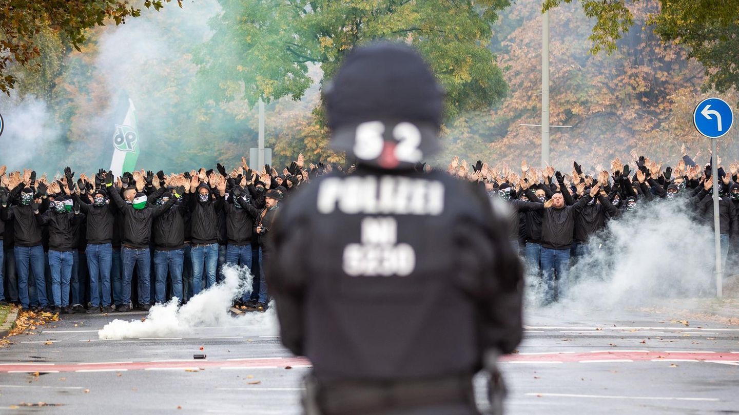 DFL muss zahlen / Rückansicht eines Polizisten vor einer Gruppe von Fußballfans