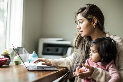 Eine Alleinerziehende sitzt mit ihrer Tochter auf dem Schoss am Laptop