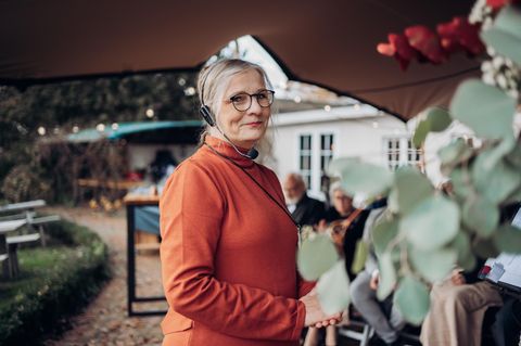 Traurednerin Kathrin Remé im kürbisfarbenen Oberteil mit Headset auf einer Hochzeit.