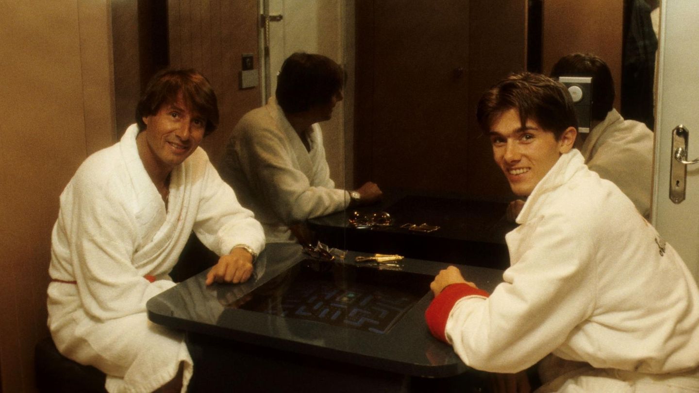 Udo Jürgens und sein Sohn John in Bademänteln beim Spielen an einem Pac-Man-Tisch