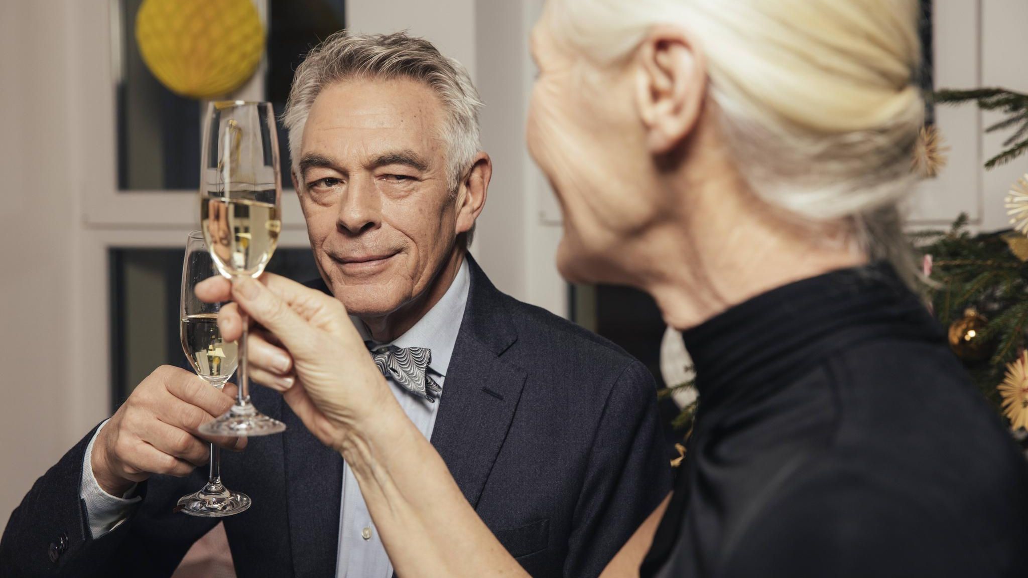 Flirten Ein Mann mit grauen Haaren und Sektglas in der Hand flirtet mit der Dame neben sich.