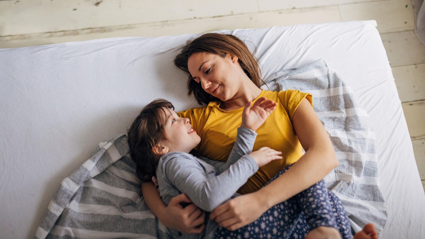Eine Mutter kuschelt morgens mit ihrem Kind im Bett