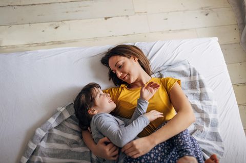Eine Mutter kuschelt morgens mit ihrem Kind im Bett