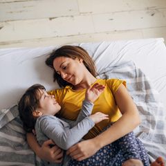 Eine Mutter kuschelt morgens mit ihrem Kind im Bett