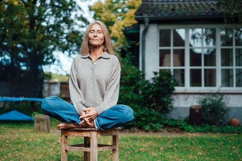 Achtsamkeit lernen: Eine Frau meditiert im Garten.