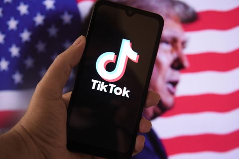 Tiktok auf einem Handy, vor einer US-Flagge mit Donald Trump