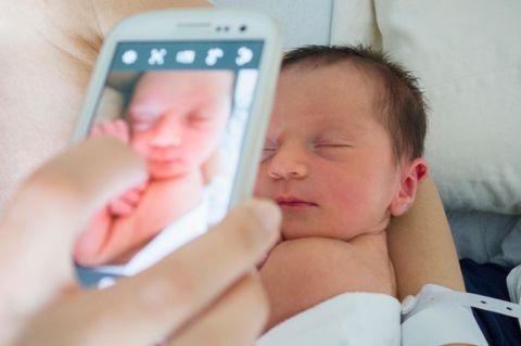 Eine Mutter fotografiert ihr Neugeborenes mit dem Handy