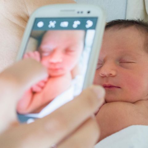 Eine Mutter fotografiert ihr Neugeborenes mit dem Handy