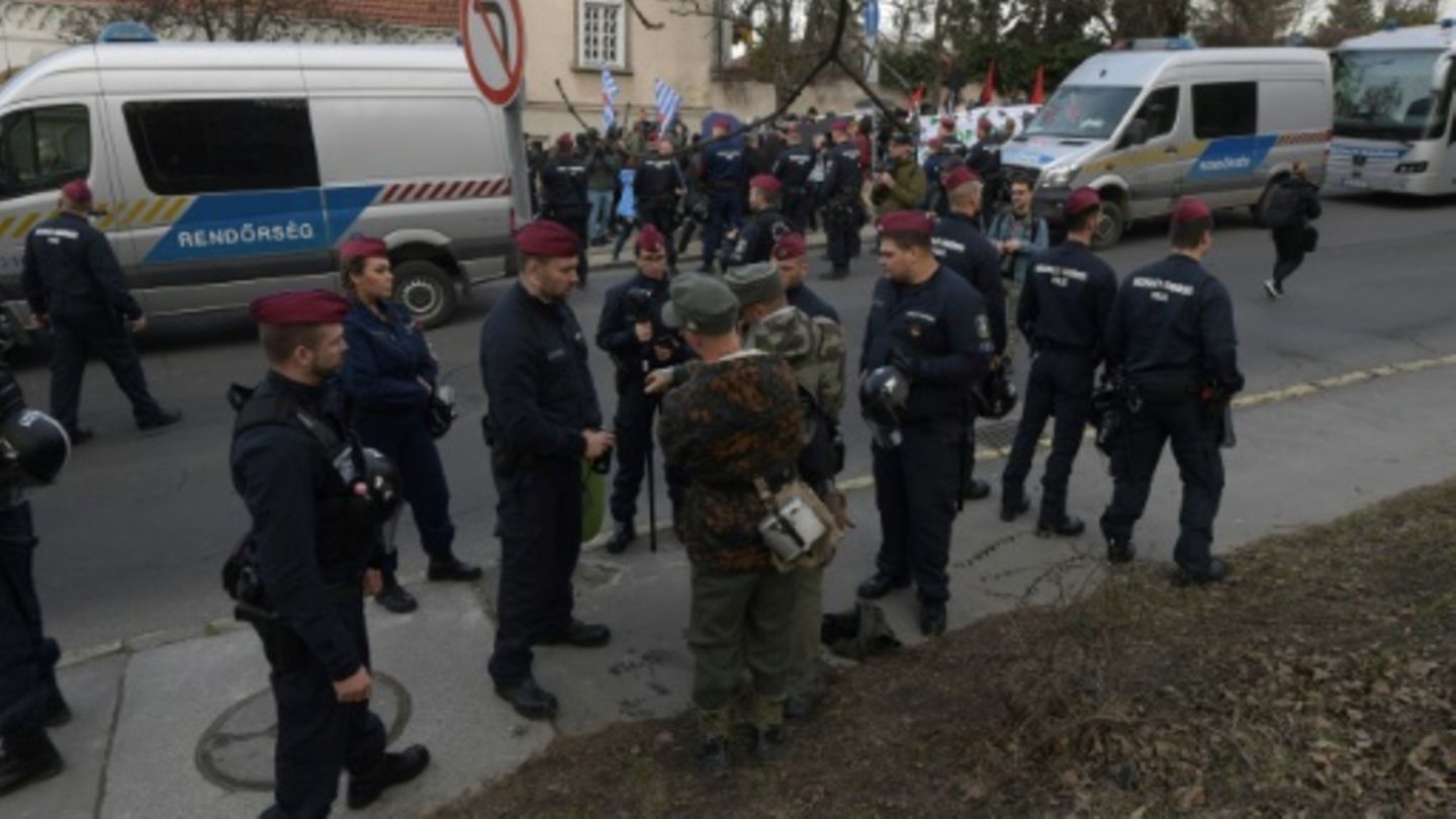 Männer in Uniformen und Gegendemonstranten beim Tag der Ehre 2024