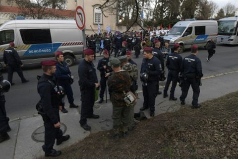 Männer in Uniformen und Gegendemonstranten beim Tag der Ehre 2024