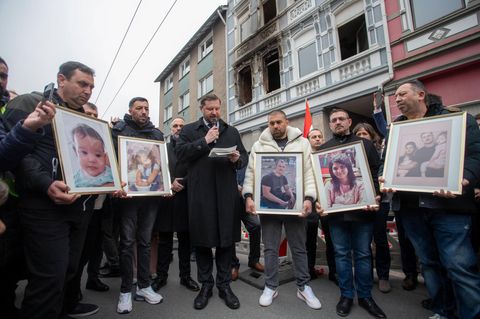 Opferangehörige halten bei einer Gedenkveranstaltung vor dem Brandhaus Fotos der Verstorbenen hoch