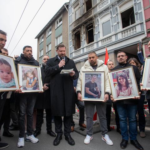 Opferangehörige halten bei einer Gedenkveranstaltung vor dem Brandhaus Fotos der Verstorbenen hoch