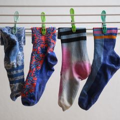 In einer Nahaufnahmen hängen vier bunte Socken auf einem Wäschestände und sind mit Wäscheklammern befestigt
