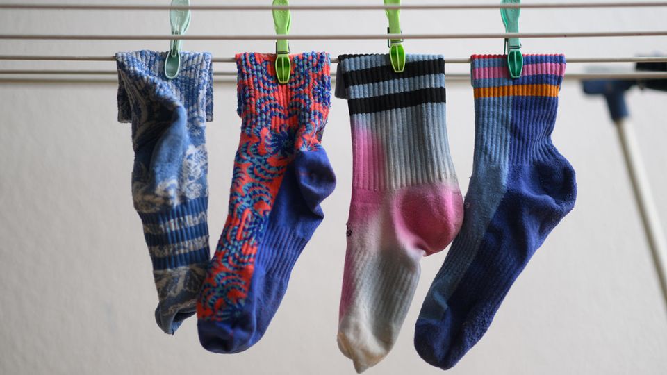 Hier trocknet frisch gewaschene Wäsche im Winter am schnellsten In einer Nahaufnahmen hängen vier bunte Socken auf einem Wäschestände und sind mit Wäscheklammern befestigt