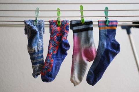 In einer Nahaufnahmen hängen vier bunte Socken auf einem Wäschestände und sind mit Wäscheklammern befestigt