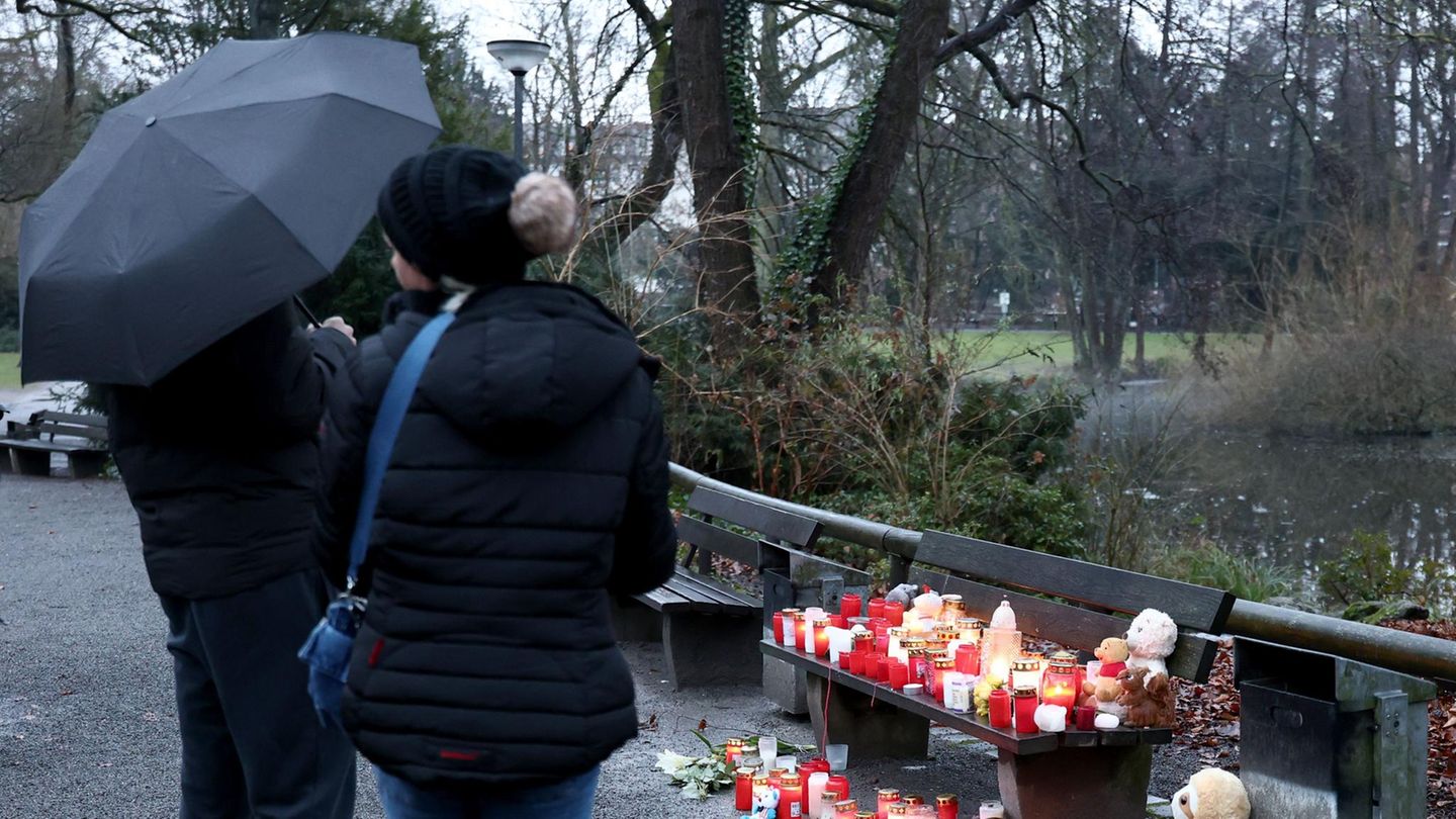 In Aschaffenburg stehen zwei dunkel gekleidete Personen vor einer Parkbank, auf der Grablichte stehen