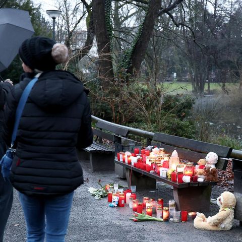 In Aschaffenburg stehen zwei dunkel gekleidete Personen vor einer Parkbank, auf der Grablichte stehen