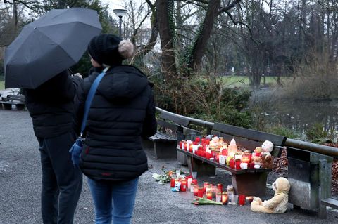 In Aschaffenburg stehen zwei dunkel gekleidete Personen vor einer Parkbank, auf der Grablichte stehen