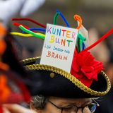 Eine Demonstrantin trägt einen Karnevalshut mit einem Schild "Kunterbunt ist besser als braun"
