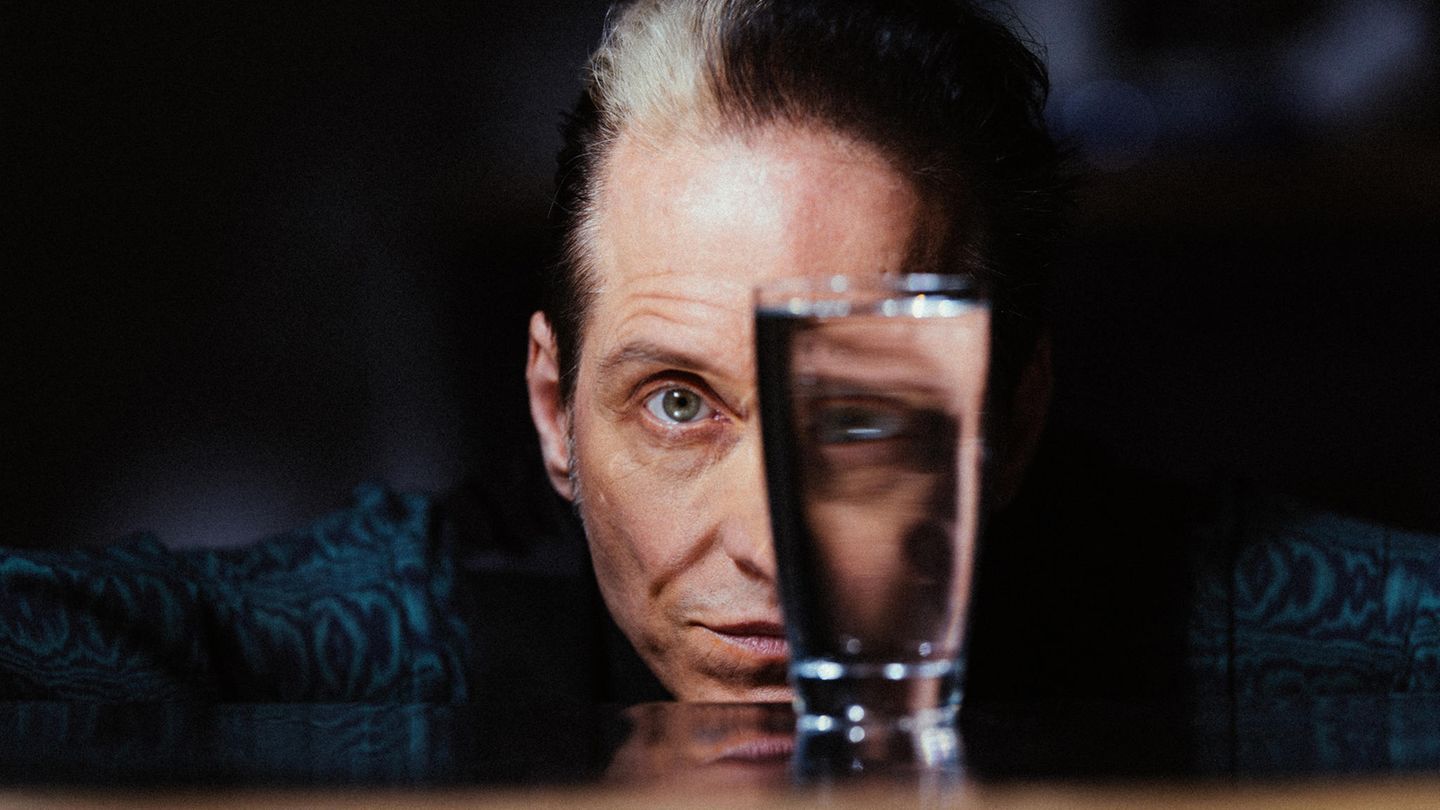 Bela B im Portrait. Vor seinem linken Auge steht ein Glas, durch das er blickt Bela B im Portrait. Vor seinem linken Auge steht ein Glas, durch das er blickt
